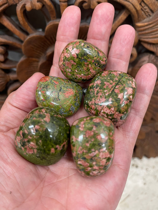 A hand holding several polished Unakite tumbled stones with a pattern of green and pink speckles.