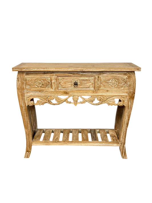 A white washed teakwood console table with floral patterns and a lower shelf, featuring three drawers and a central rectangular tabletop.