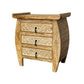 A white washed teak wood nightstand with three drawers, featuring intricate carvings on the front and a curved design at the top.